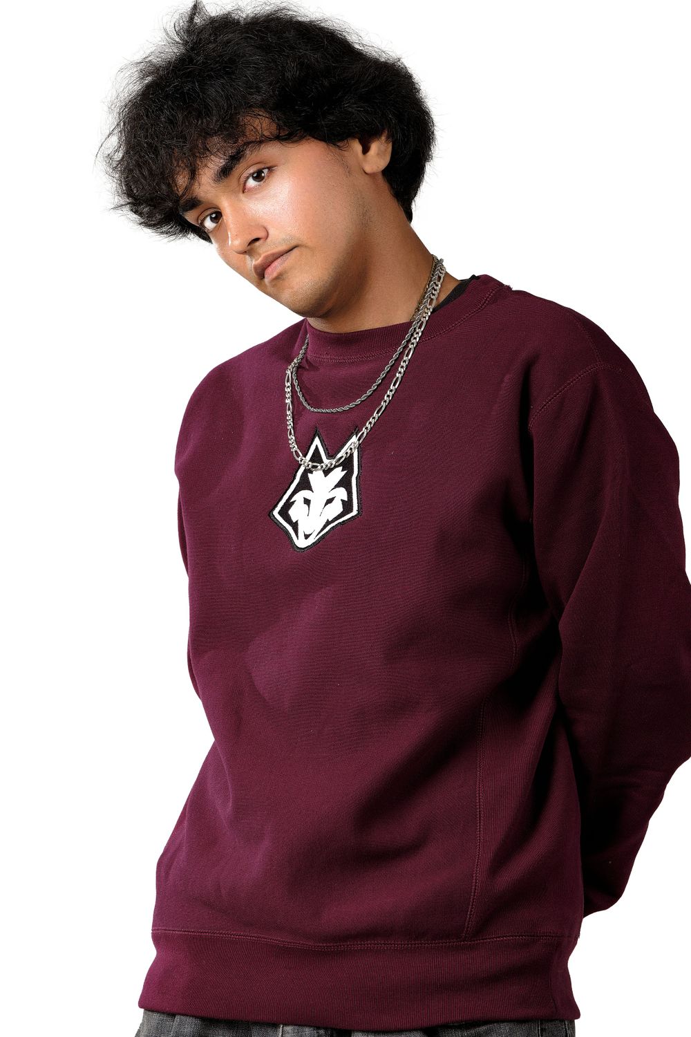 Person wearing burgundy sweatshirt with chain necklace and logo detail.