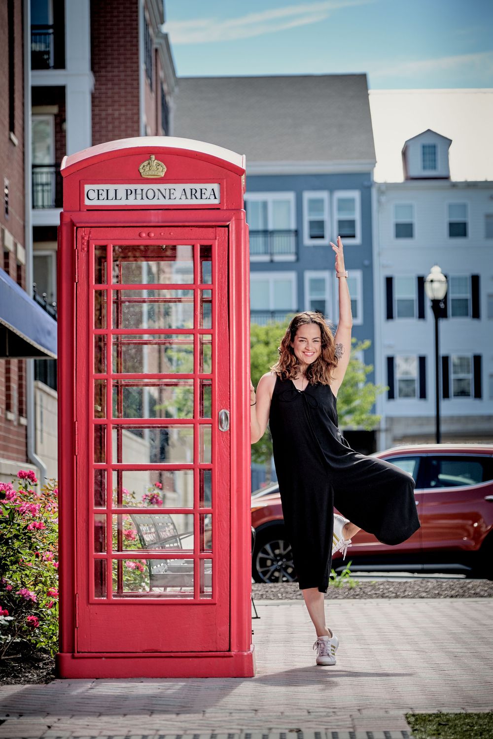 A red British-style phone booth labeled 'Cell Phone Area' stands in front of brick buildings on a sunny day.