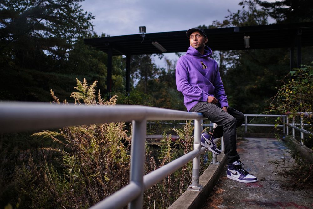 Person in purple hoodie sitting on metal railing at dusk with trees in background.