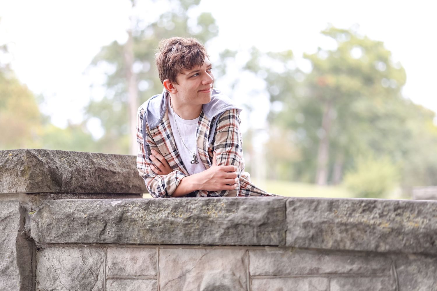 Senior leans on a stone bridge while smiling off to the side
