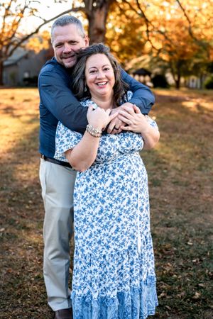 Couple embracing outdoors during golden hour with colorful fall foliage in background.