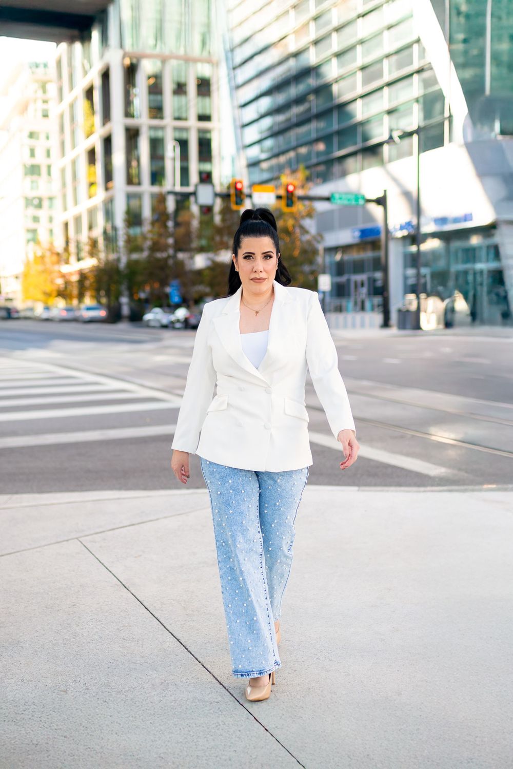 A stylish street fashion look featuring a crisp white blazer paired with light wash jeans on a city sidewalk.