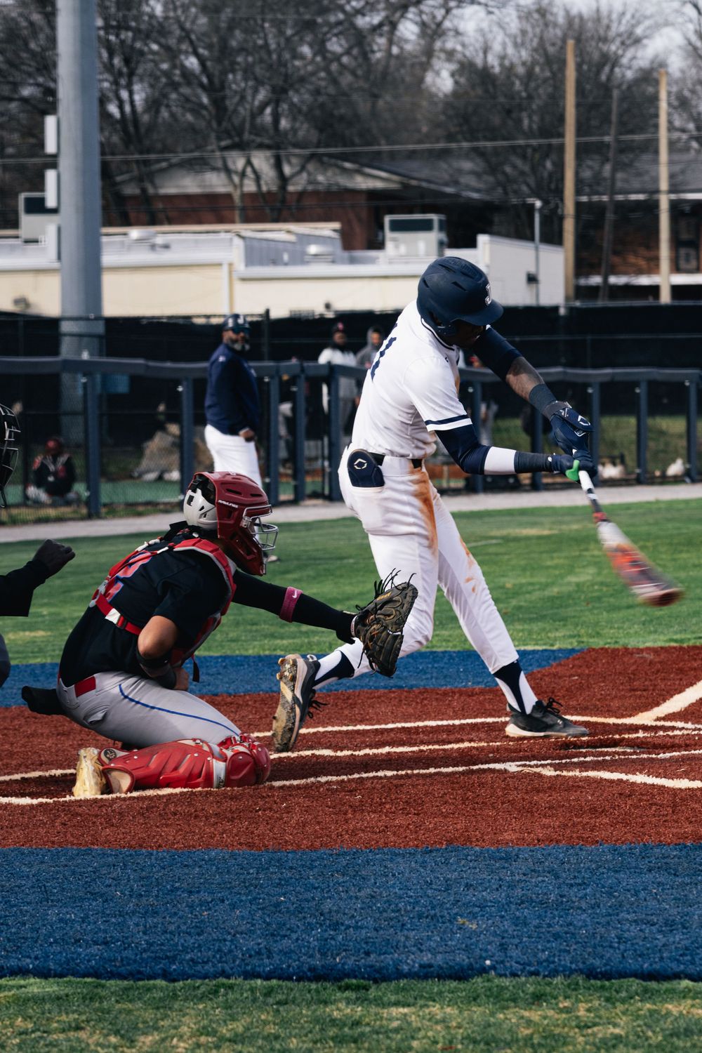 Baseball player sliding into base during a game on red clay infield with blue warning track.
