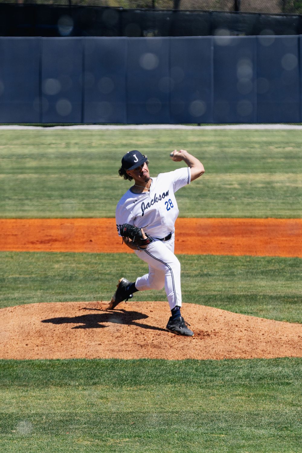 Baseball pitcher in white uniform winds up to throw from the mound during a sunny day game on a well-maintained field.