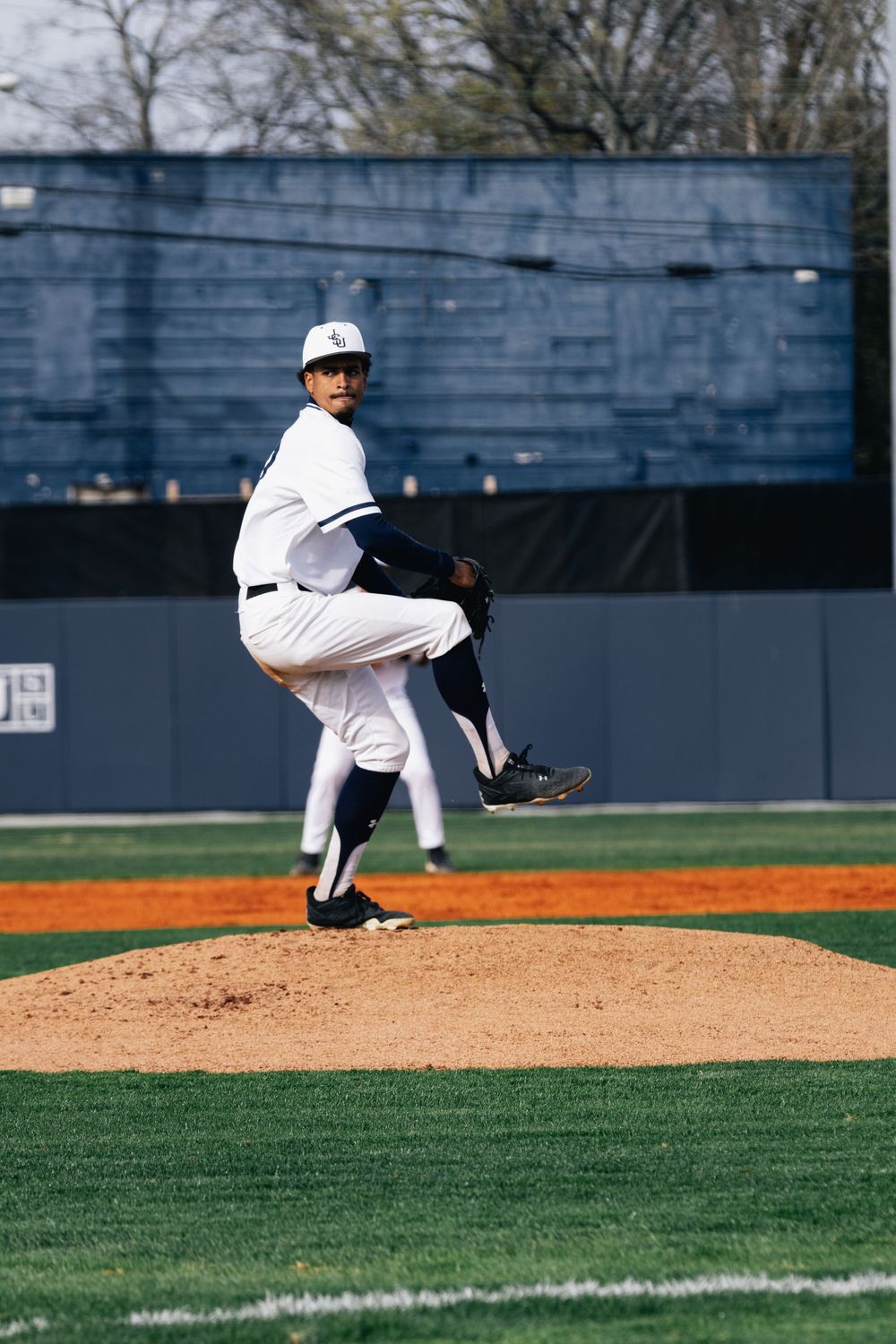 Baseball pitcher in white uniform winds up for pitch on mound during game.
