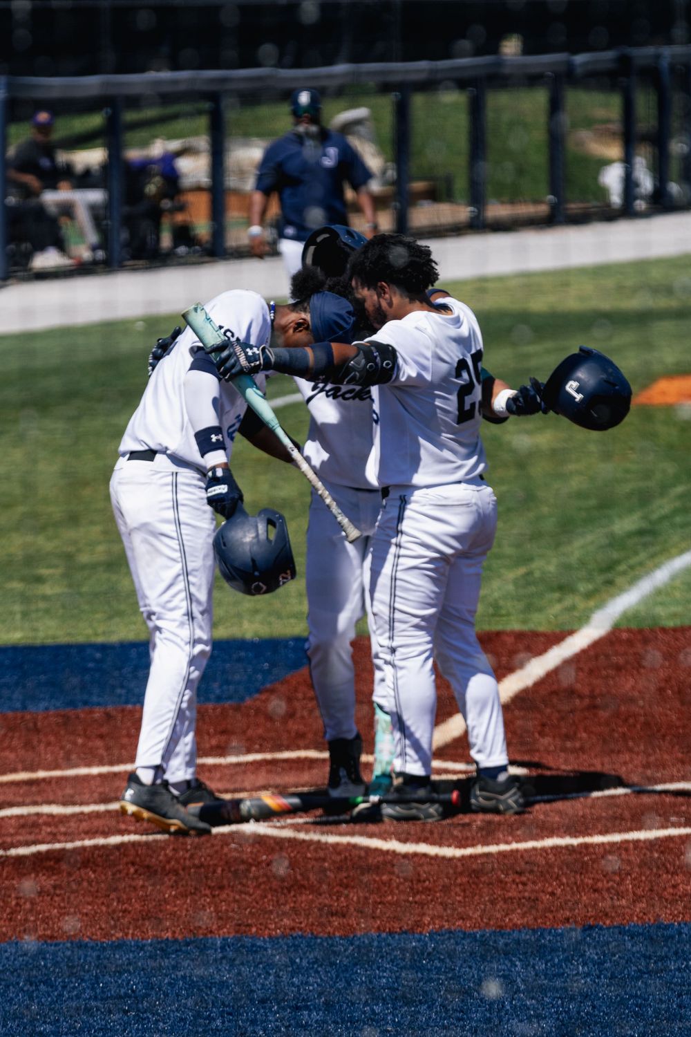 Baseball players in white uniforms bow to each other at home plate before a game on a sunny day.