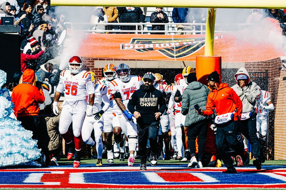 College football team in red uniforms running onto field through smoke tunnel during a sunny game day.