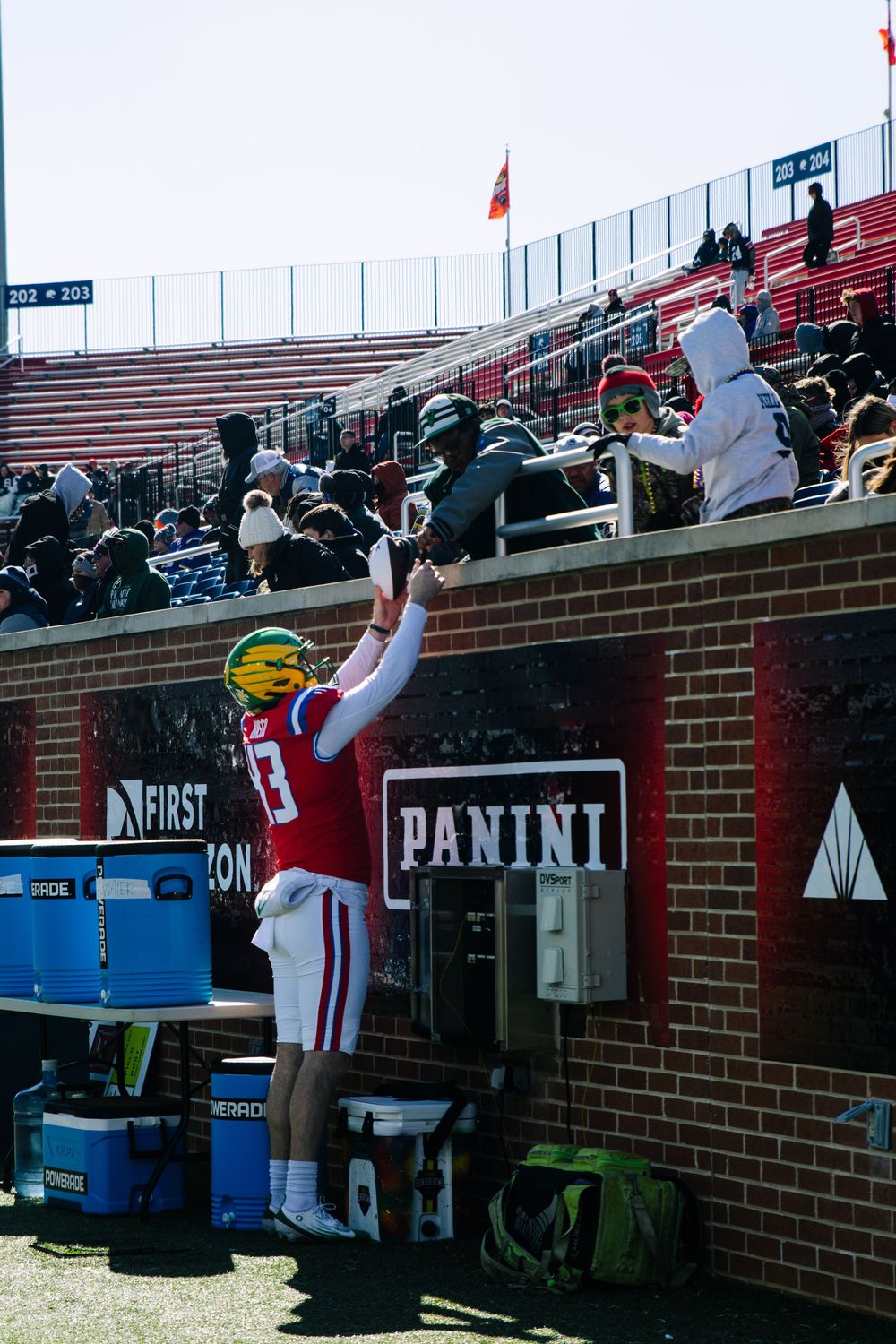 Football player in red jersey reaches up to fans in stadium stands near Panini sponsored wall on sunny day.