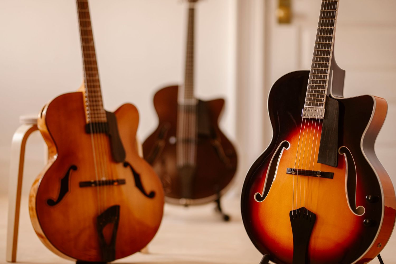 Three elegant acoustic guitars displayed against white wall showing different wood tones and styles.