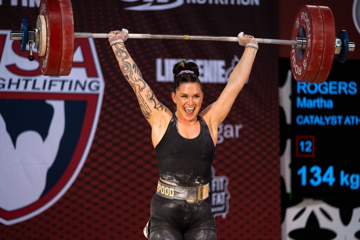 Competitive weightlifter successfully completing overhead lift of 134kg barbell during competition event.