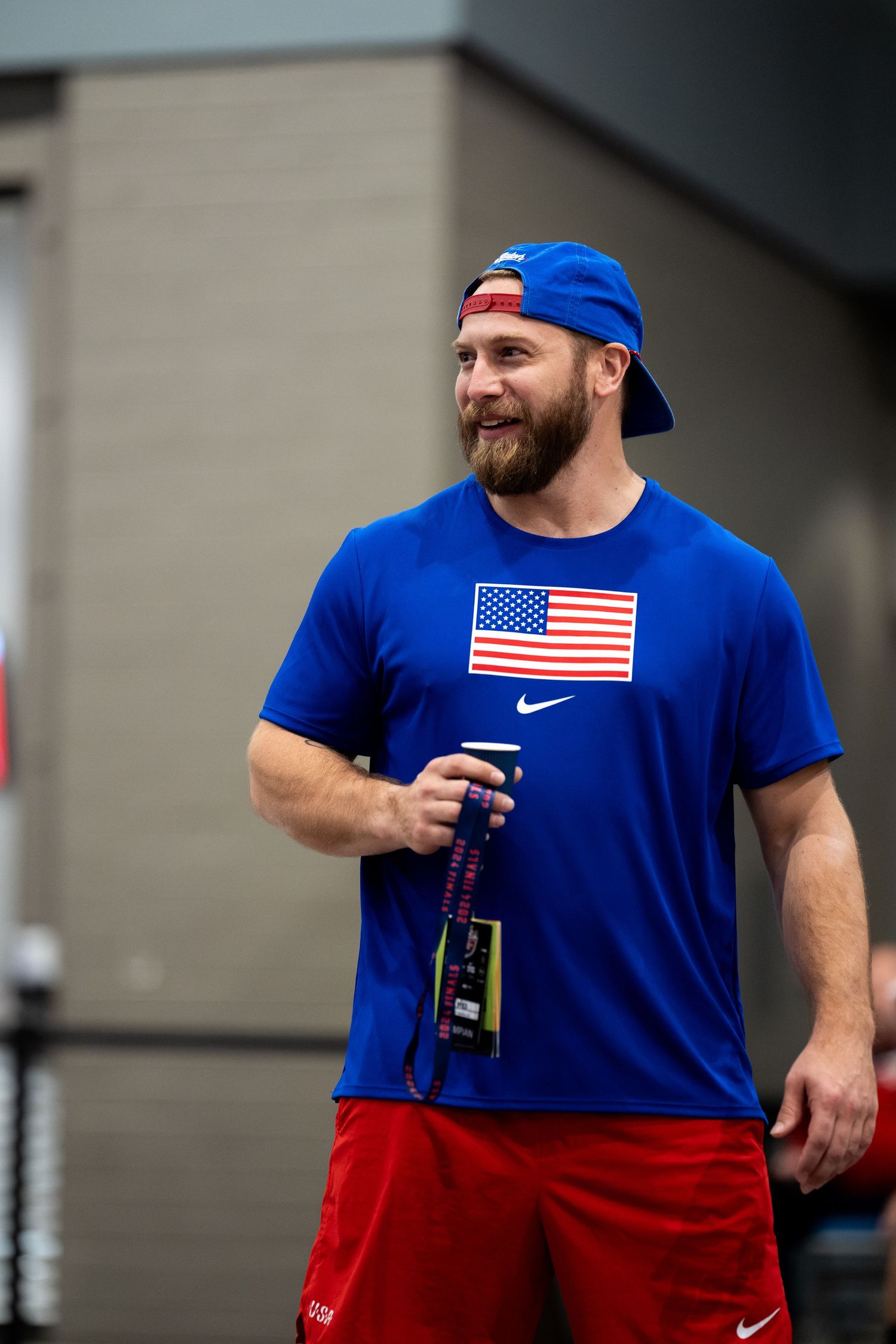 Athlete wearing USA flag Nike shirt and backwards blue cap holding water bottle at sports event.