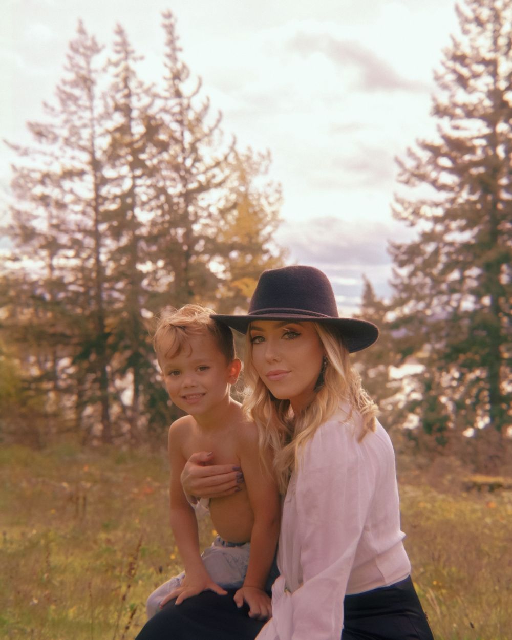 An outdoor portrait of mother and child against tall pine trees during sunset with warm autumn tones.