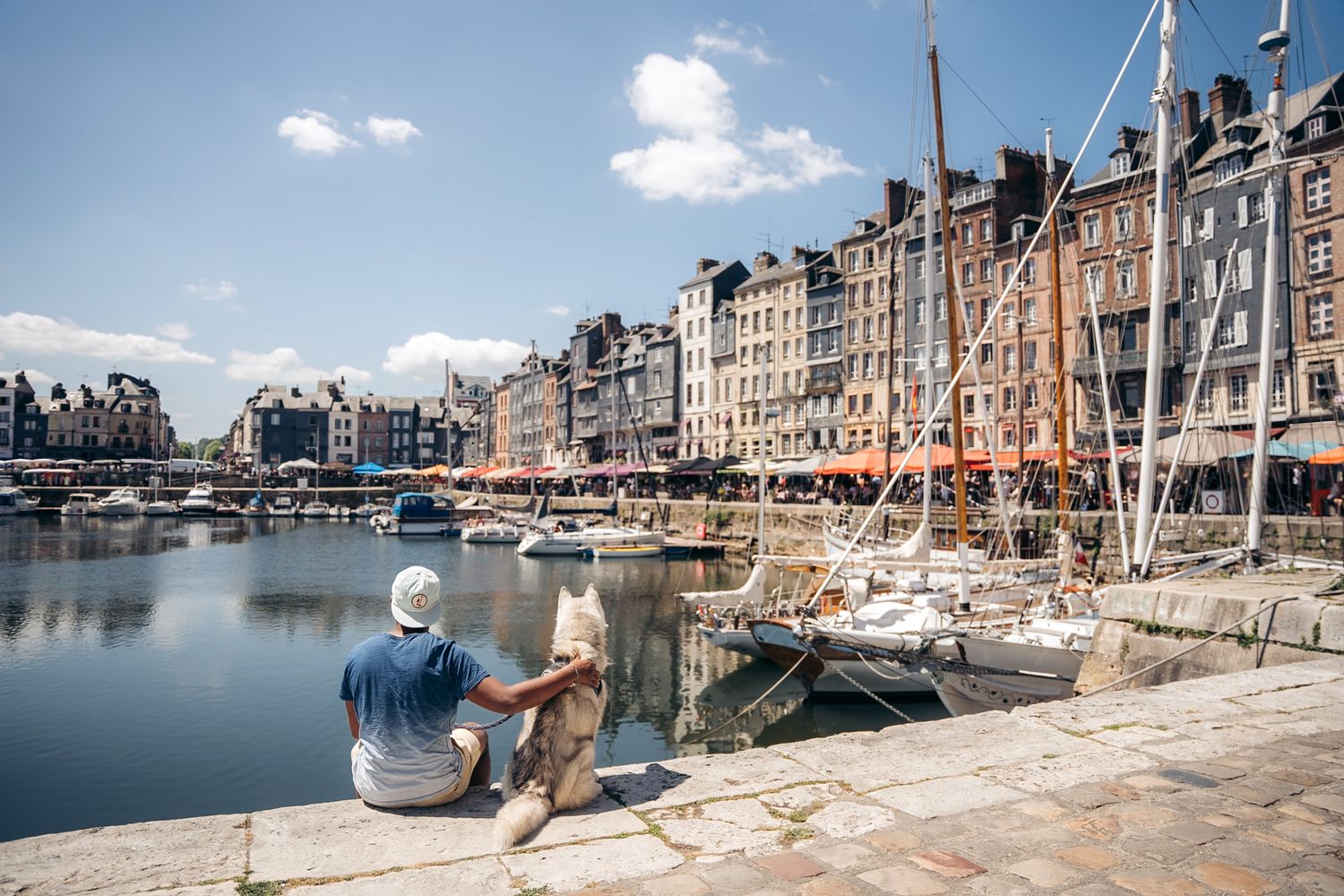 Vieux bassin de Honfleur avec ses bateaux et son centre historique. Un vacancier regarde le port et les terrasses de restaurant en été