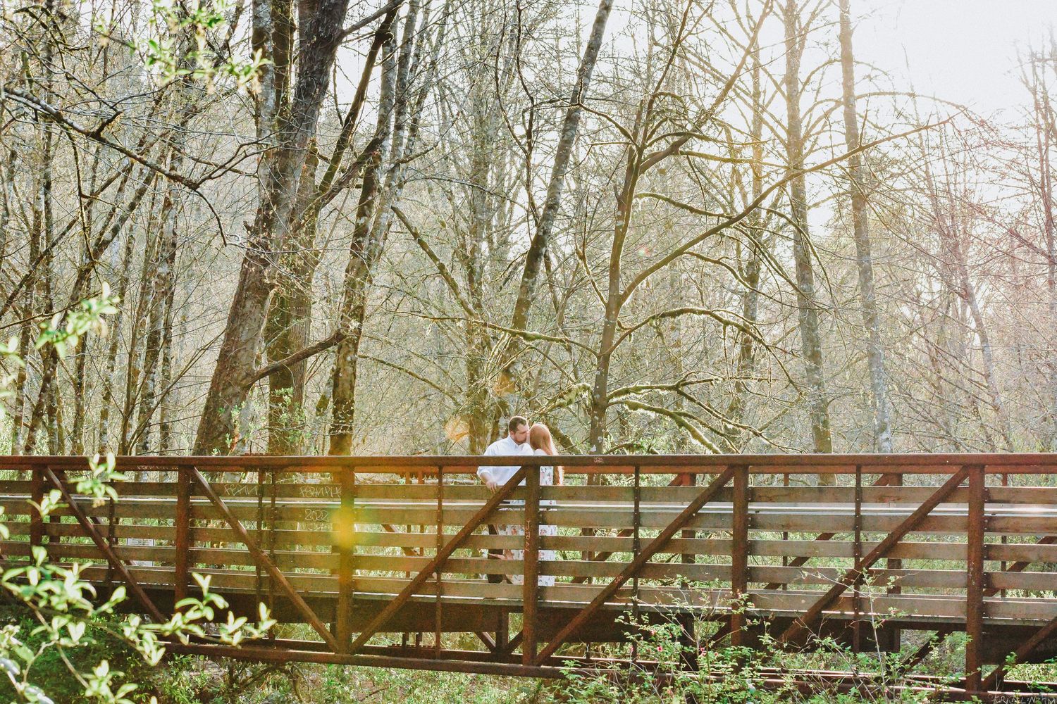 Couple embracing on a wooded trail during a spring engagement session in the Pacific Northwest. Natural light and rustic forest backdrop add