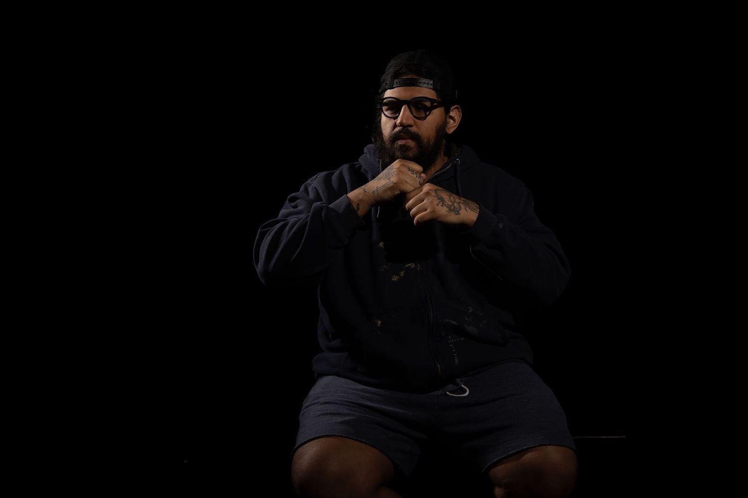 A dark portrait of Ken with him playing with his beard