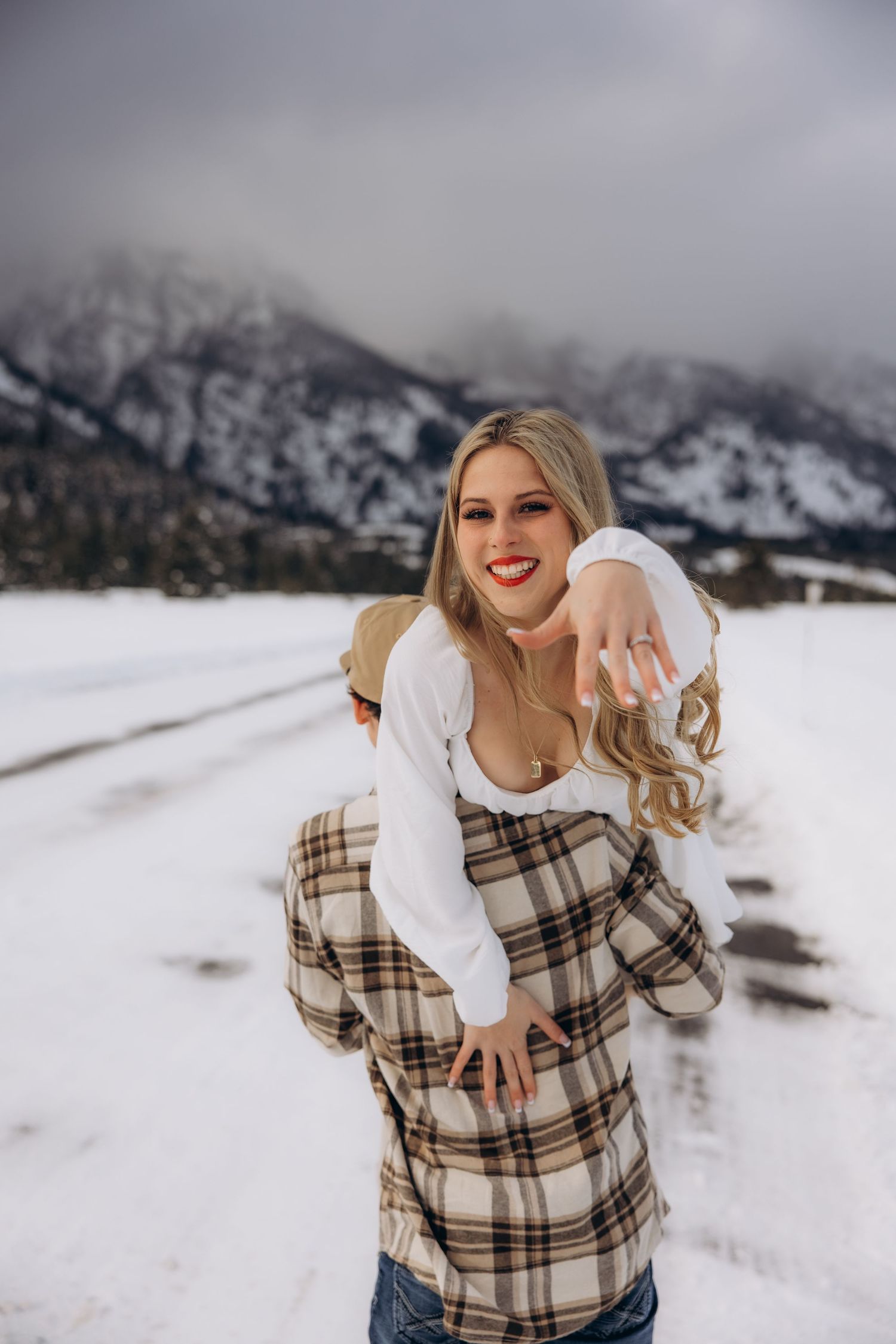 An engaged couple celebrates in a snowy mountain landscape as they show off an engagement ring at Jackson hole, Wyoming. Photographer: Nora