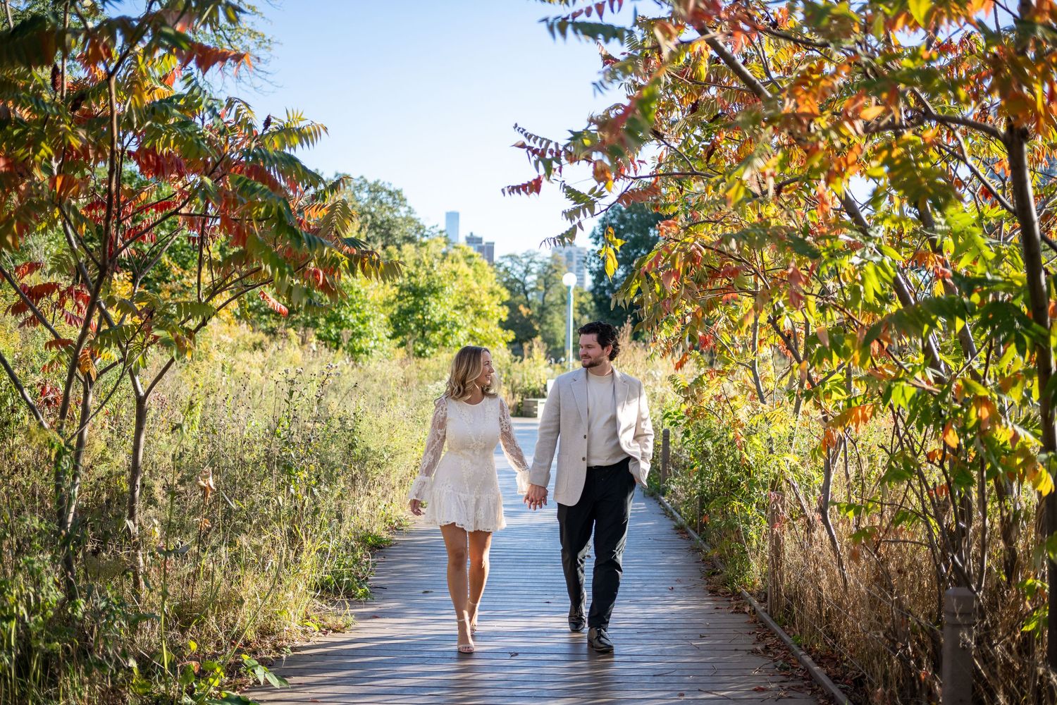 Engagement photo of couple walking through fall leaves at South Pond in Lincoln Park.