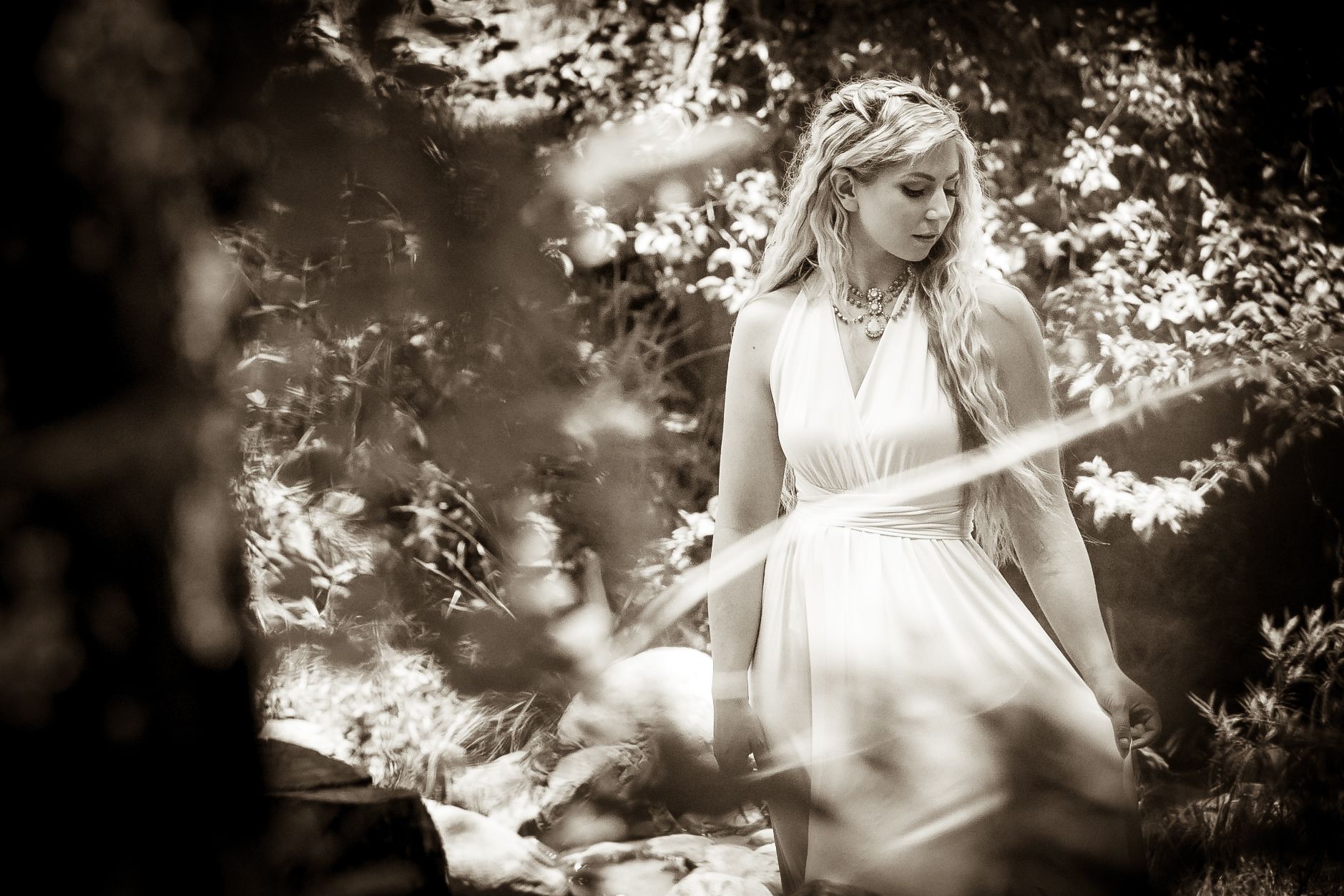 Ethereal black and white portrait of a figure in a white dress among sunlit trees.
