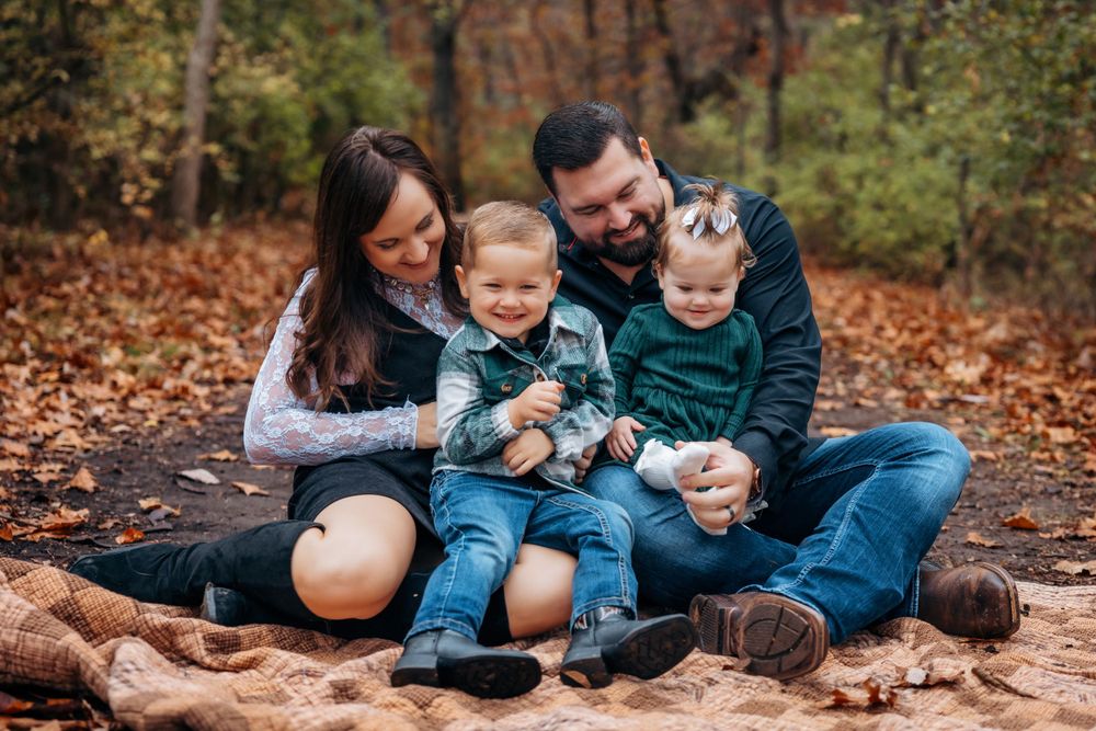 Family of four sits together on rocks surrounded by fallen autumn leaves.