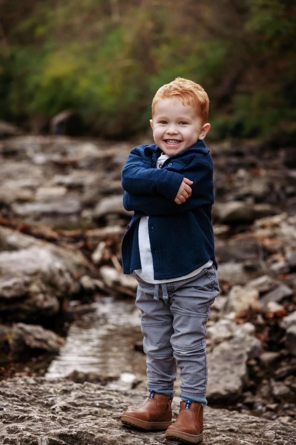 A young child in a navy jacket and brown boots standing confidently on rocky terrain.