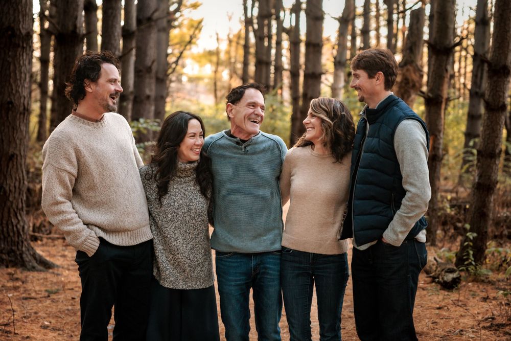 A group laughing together in cozy sweaters during a sunset forest photoshoot.