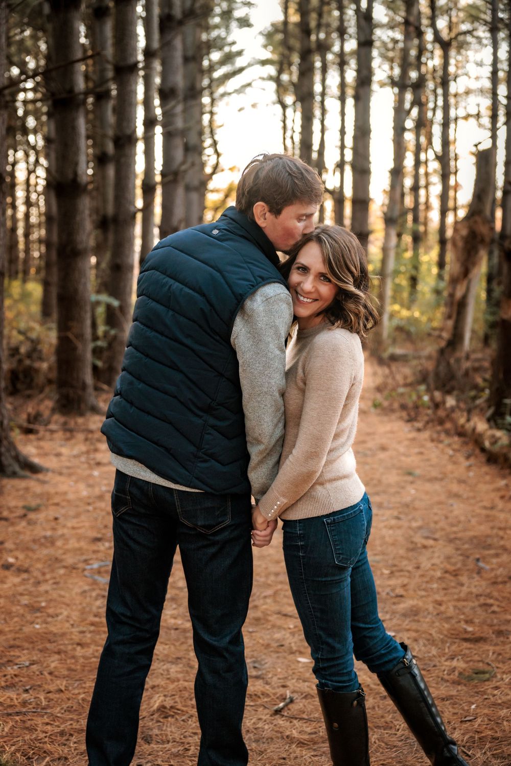 A romantic couple embracing on a forest trail during golden hour sunset.