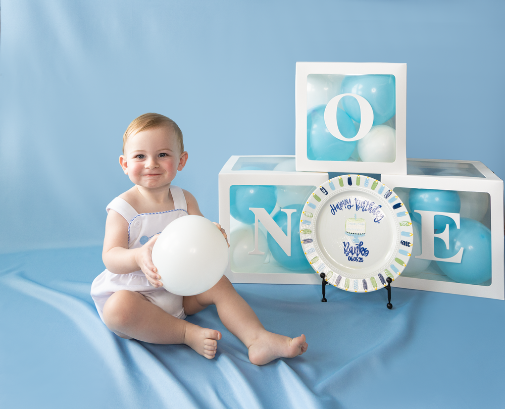 Smiling baby boy sitting with white balloon beside ONE letter blocks for first birthday photo session.