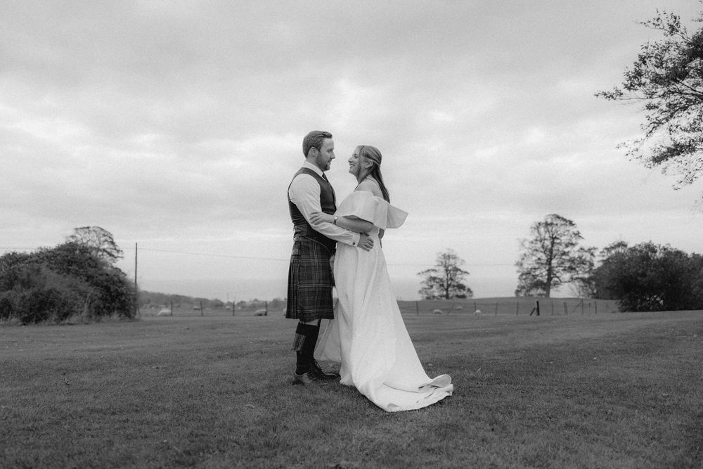 A romantic black and white wedding photo series showing a couple embracing in a scenic outdoor landscape.
