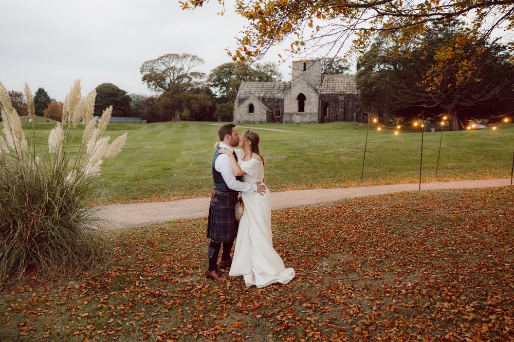 A couple embraces in a romantic autumn scene with fallen orange leaves scattered across the ground.