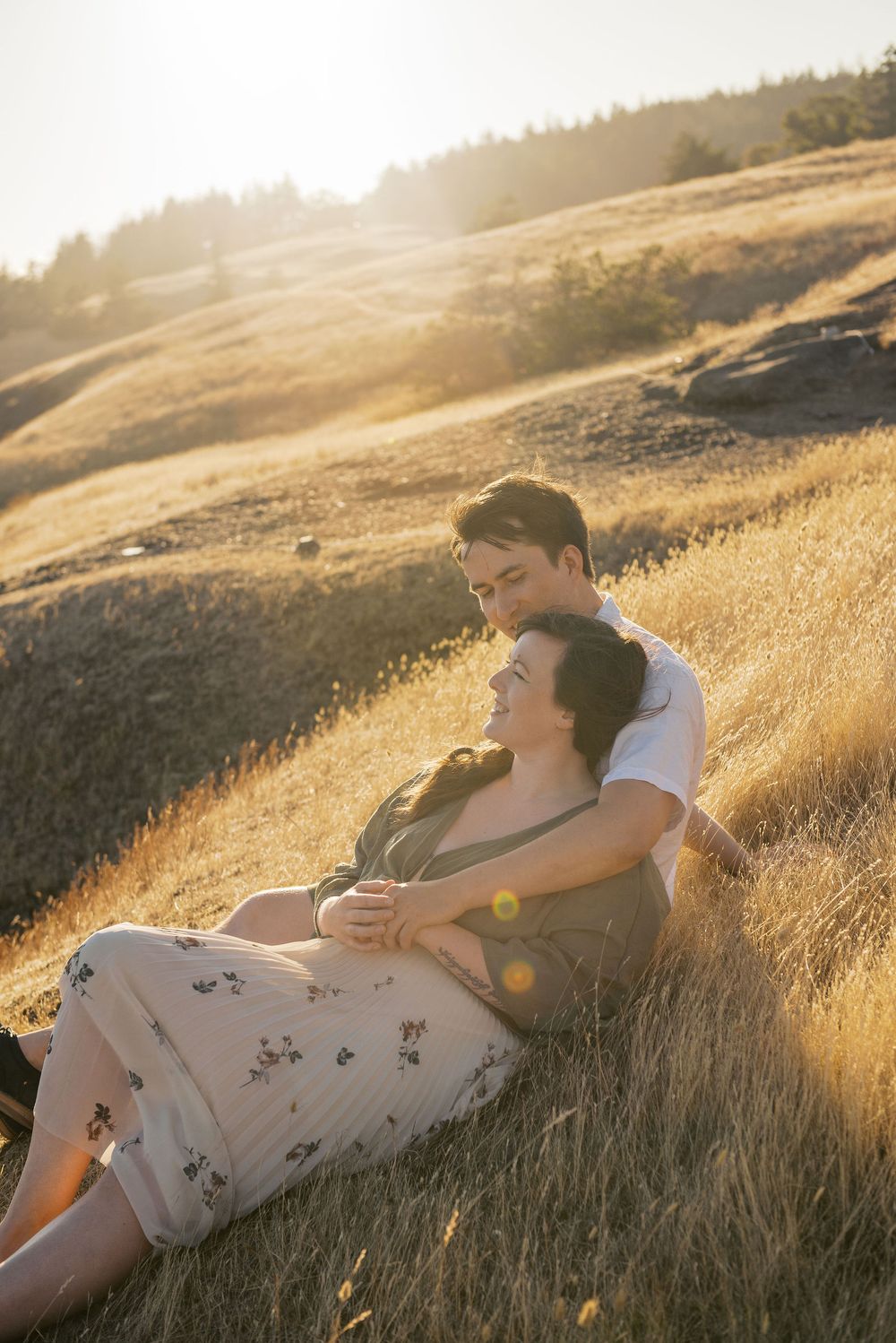 A person in a floral dress lies peacefully in golden sunlit grass during sunset on a hillside.