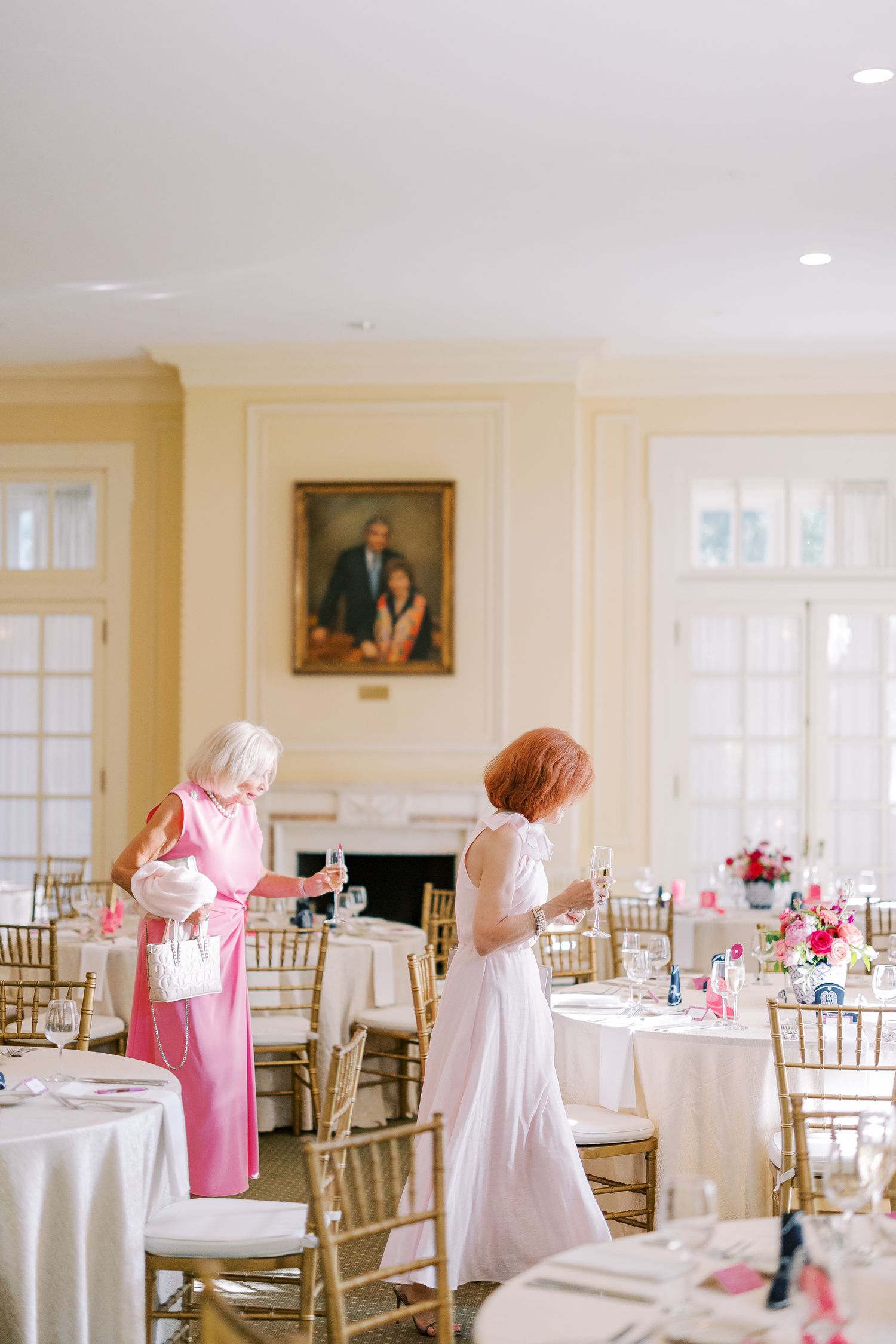Elegant wedding reception venue with white tablecloths, gold chiavari chairs, and pink floral accents.