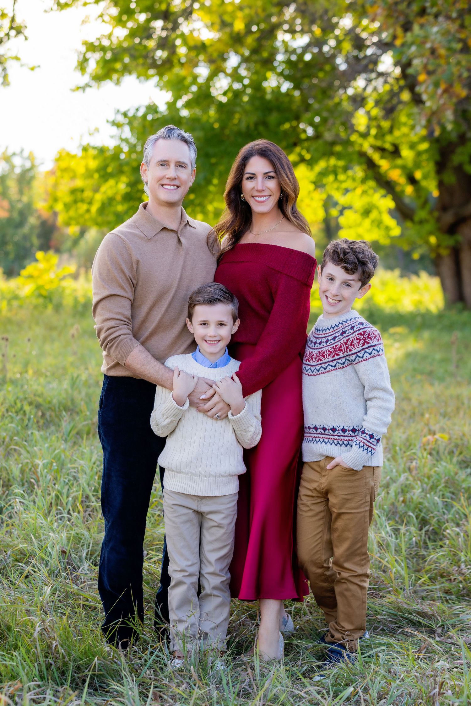 A family wearing coordinating sweaters poses together in a sunny field during an autumn photo session.