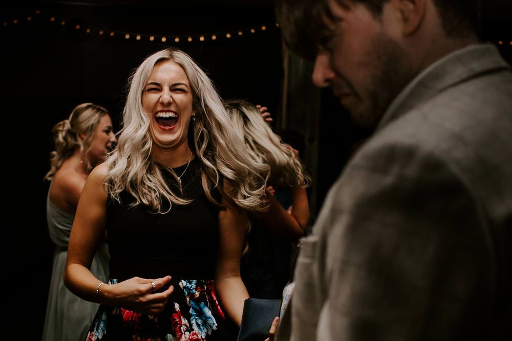 Wedding guests dance and laugh together during an evening celebration under string lights.