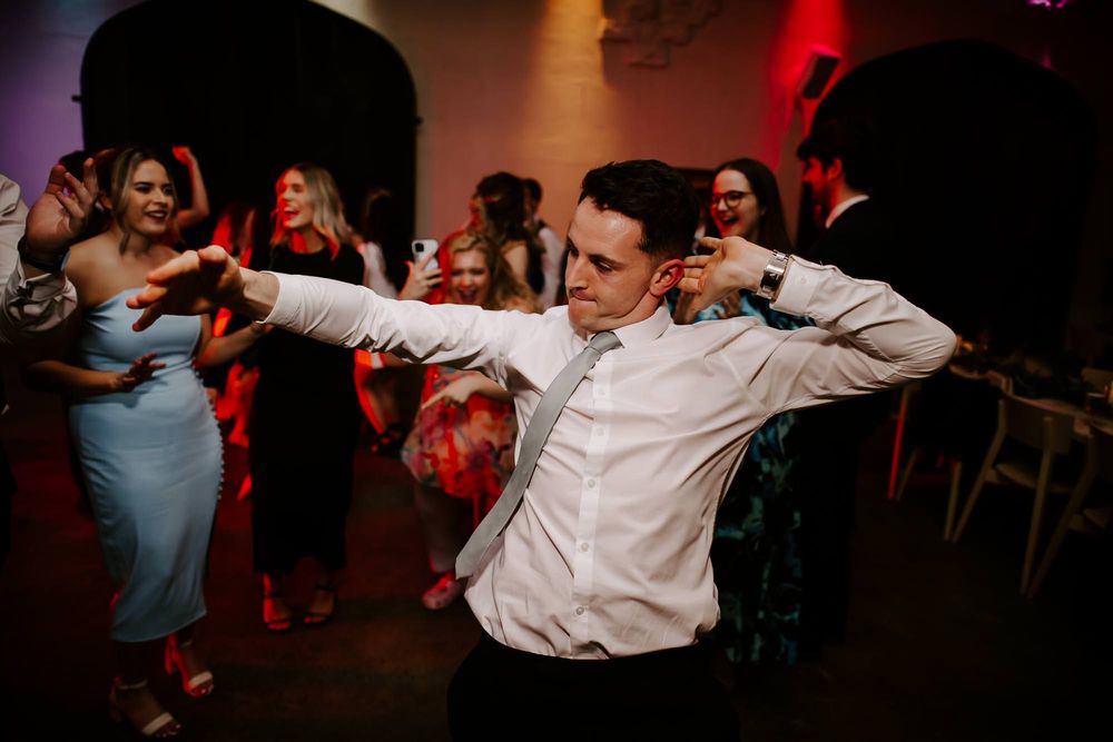 Wedding guests dance energetically on a dimly lit dance floor with red lighting effects in the background.