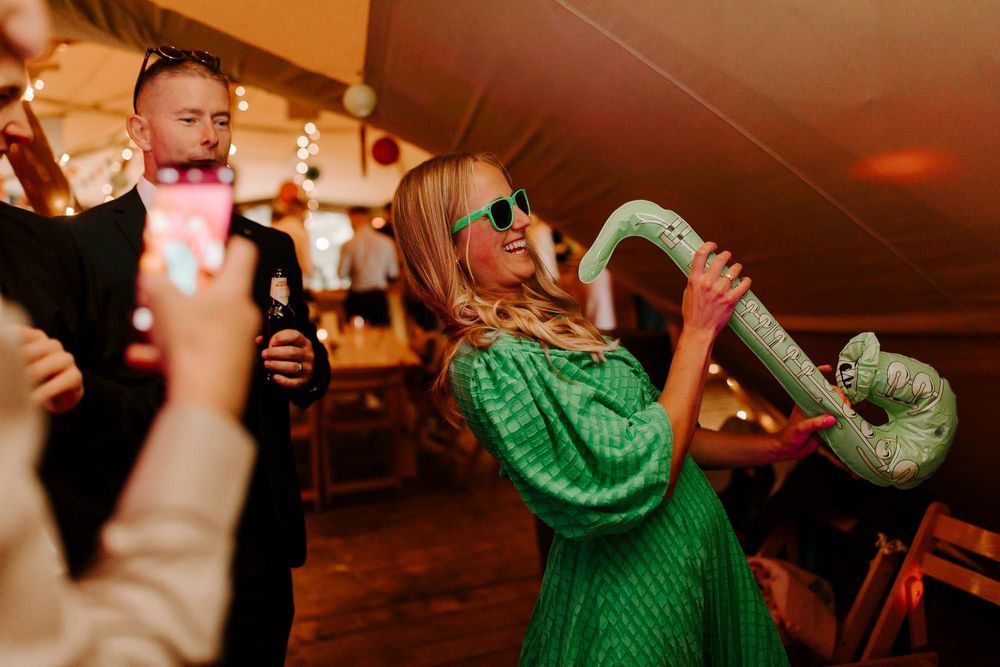 Person in bright green sweater dances enthusiastically at party while holding drink bottle under warm lighting.