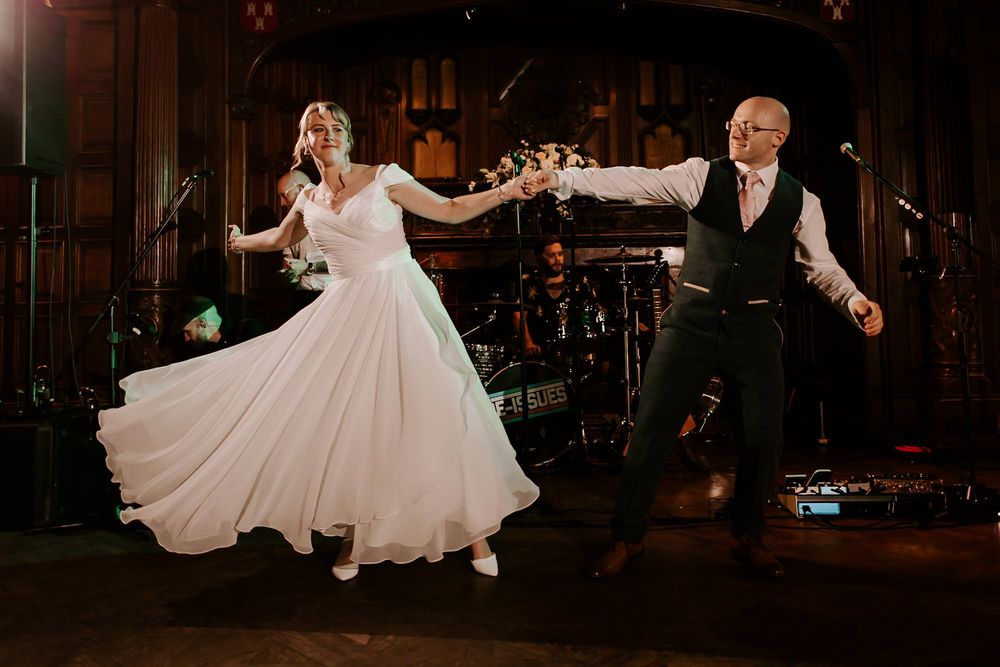 A couple in formal wedding attire dances together in a dimly lit venue with elegant lighting and decor.