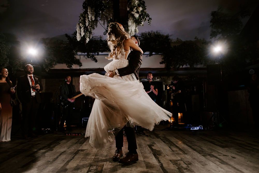 A couple in formal wedding attire dances together during their first dance at an evening reception.
