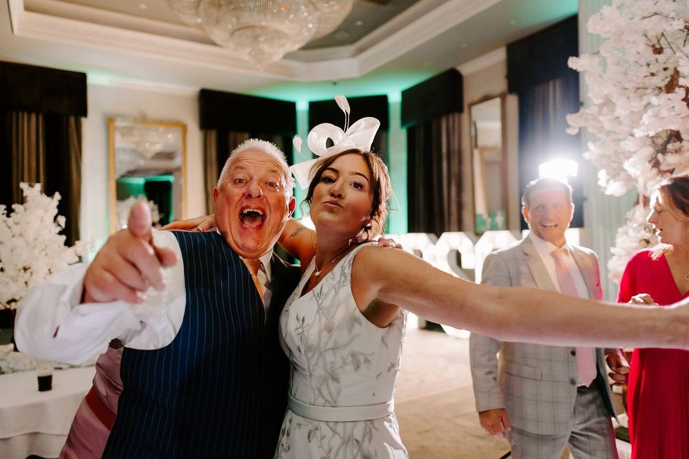 Wedding guests dance and celebrate joyfully on a crowded dance floor at an elegant indoor reception venue.
