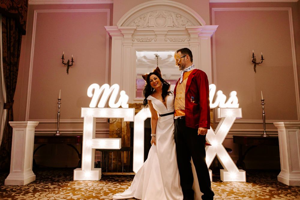 A couple dances together at their wedding reception in front of illuminated F and K letters against an elegant wall.