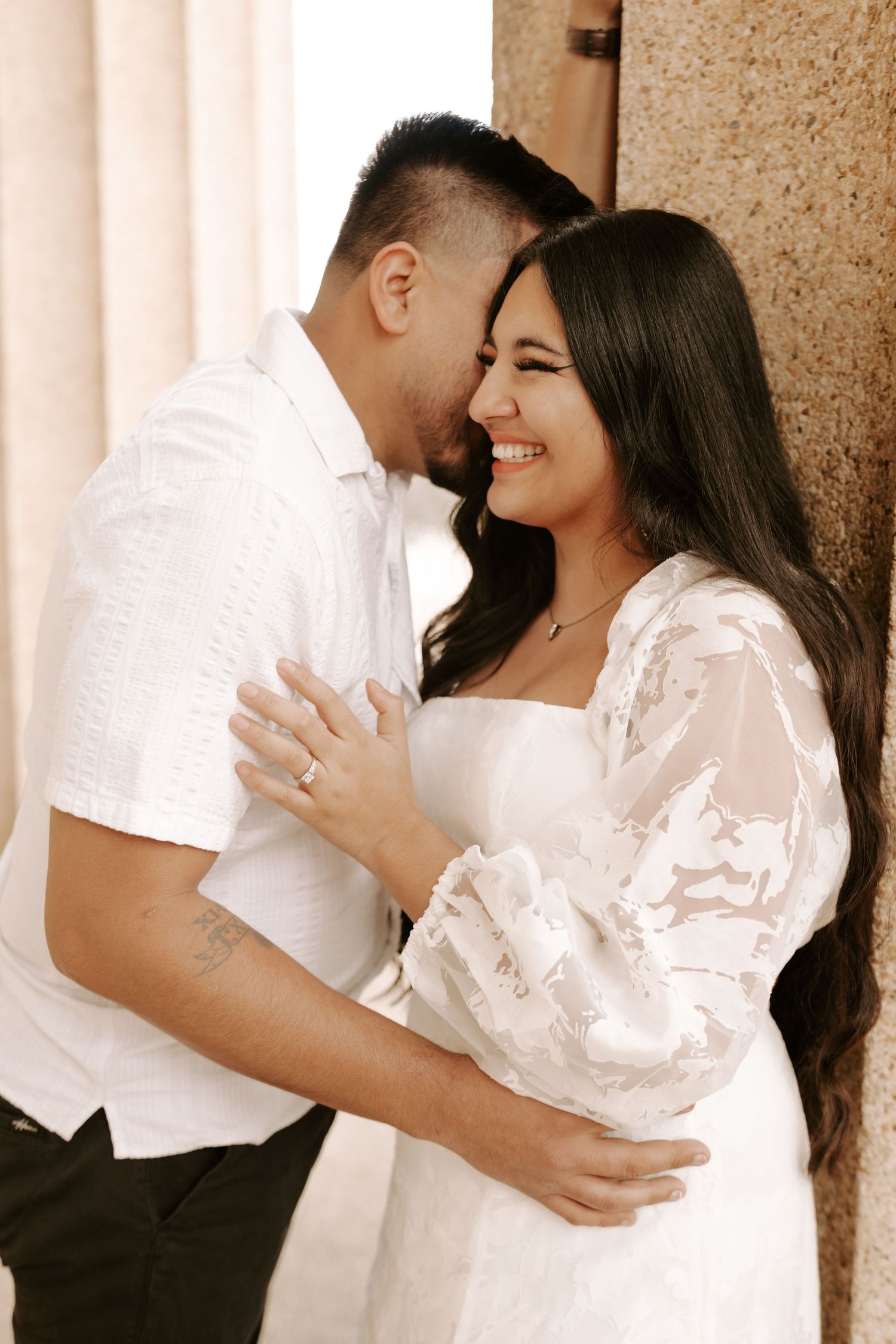 Romantic engagement photos showing a couple in white outfits embracing against a beige backdrop.