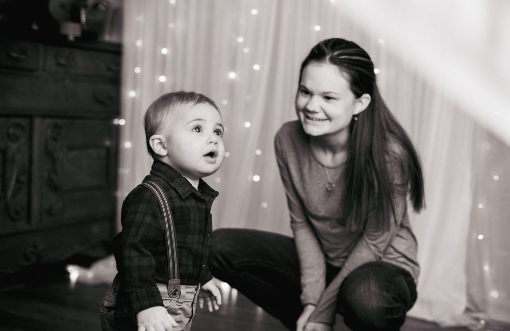 A black and white photograph of a young child in suspenders sitting with a companion against a backdrop of twinkling lights.