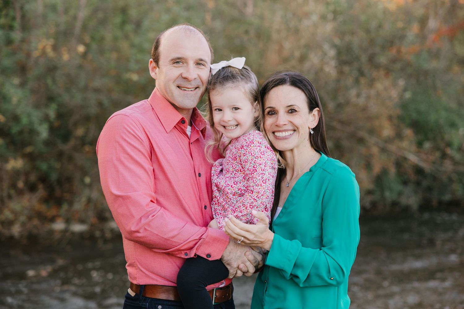 A family wearing red and plaid outfits poses together in a snowy winter setting near a stone wall.