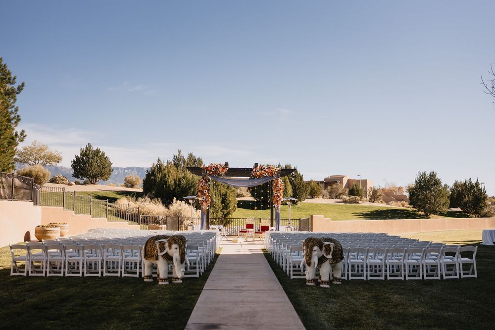 Outdoor Indian wedding ceremony setup with white chairs, floral aisle decorations, and mountain backdrop.at Sandia Resort and Casino