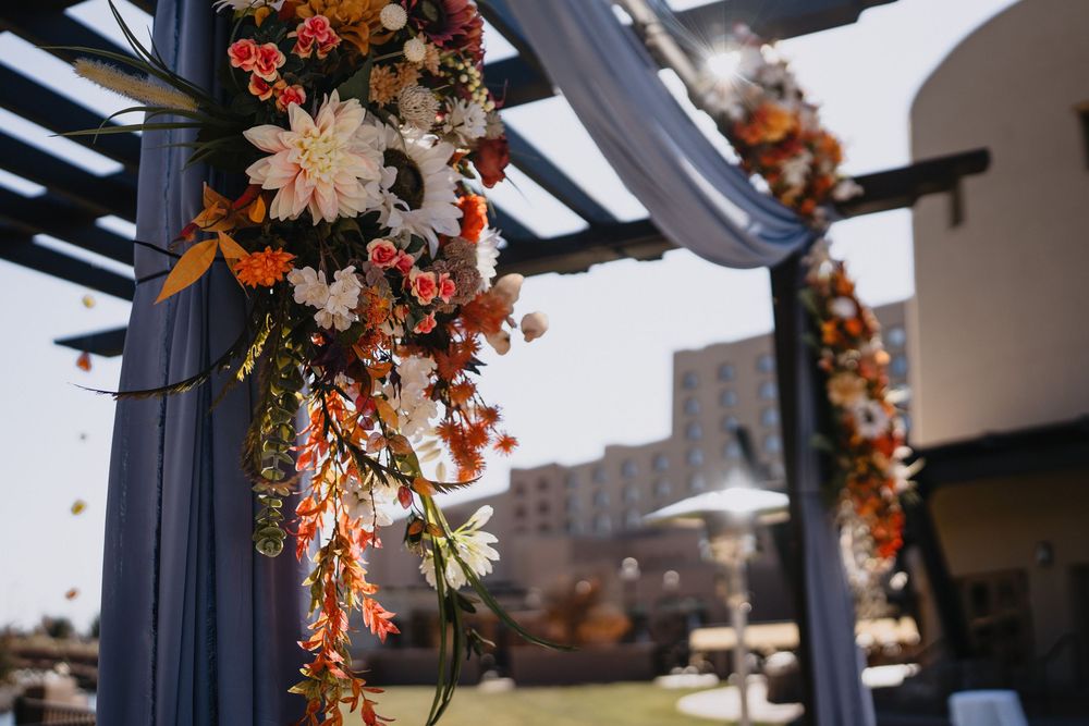 Colorful orange and white floral arrangement decorating blue draped wedding ceremony arch outdoors.at Sandia Resort and Casino