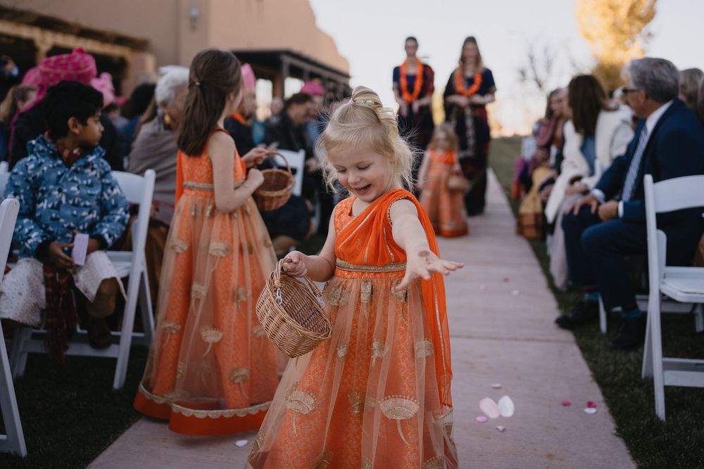 Young flower girl in orange Indian dress scattering petals along wedding ceremony aisle.at Sandia Resort and Casino