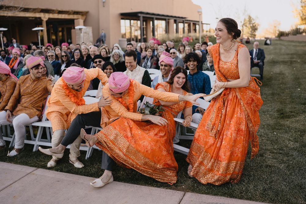 Bridesmaids in orange lehengas laugh and dance with guests during lively Indian wedding ceremony.at Sandia Resort and Casino