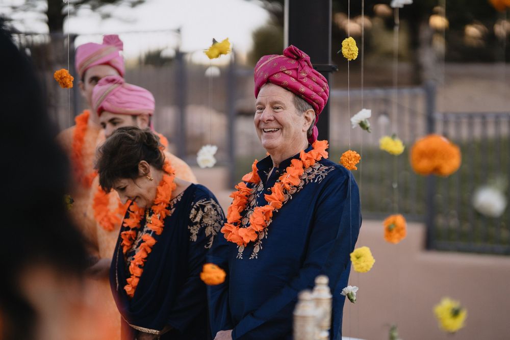 Smiling man in navy suit and pink turban with marigold garland enjoys outdoor Indian wedding ceremony.at Sandia Resort and Casino