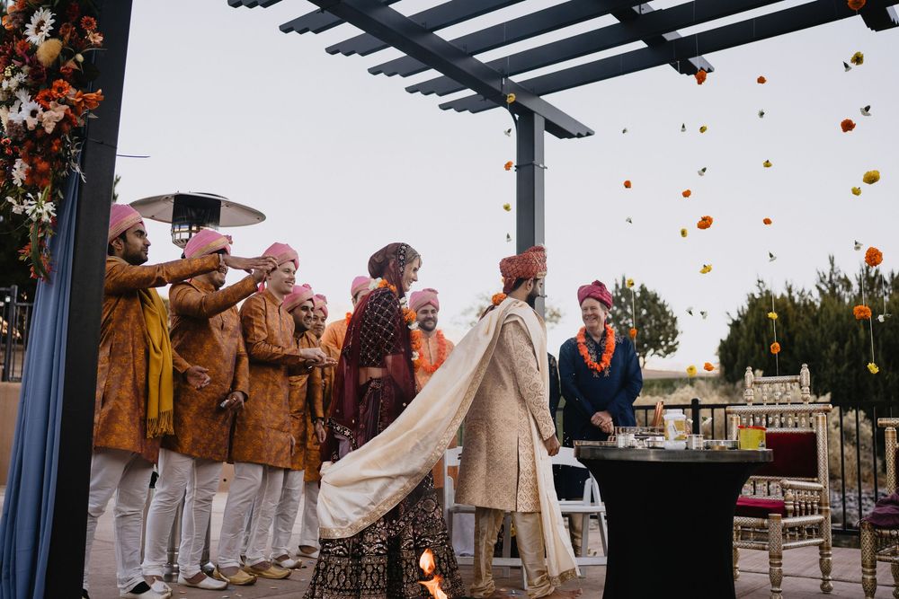 Wedding party in colorful attire gathers under pergola as flowers rain down during Hindu ceremony.at Sandia Resort and Casino