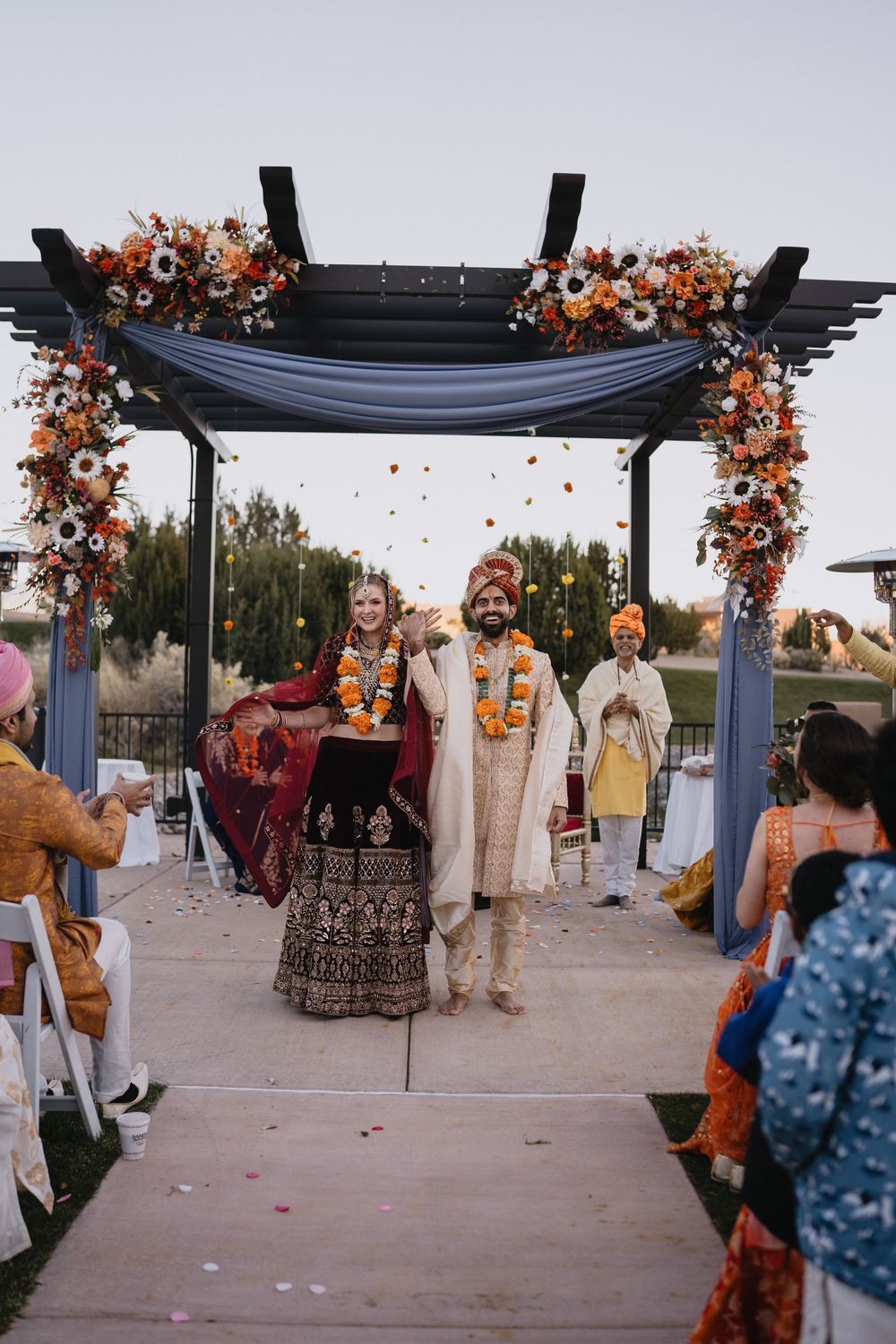 Indian bride and groom celebrating under floral arch after traditional Hindu wedding ceremony outdoors.at Sandia Resort and Casino