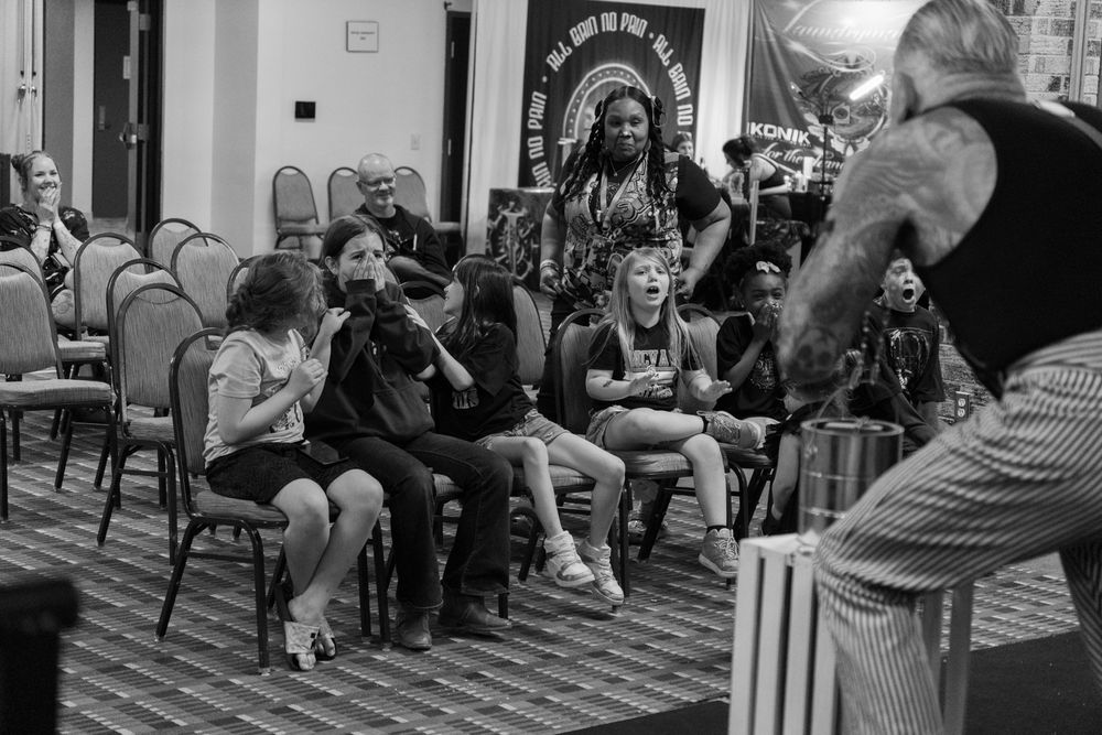 Black and white photo of children reacting with excitement during a live performance at an indoor event.